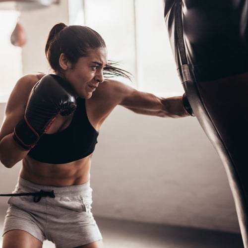 Une femme frappe avec force dans un sac de boxe en utilisant des gants de boxe.