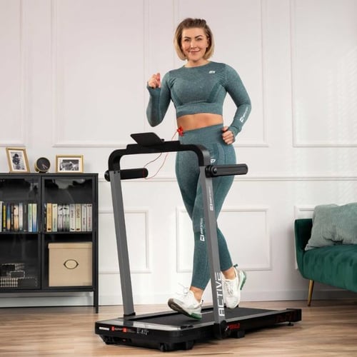Une femme en tenue de sport bleue court sur un tapis de course Hop Sport.