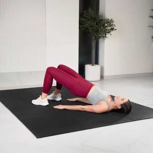 Une femme est allongée sur le dos sur un grand tapis de course, soulevant ses hanches pour travailler ses abdominaux