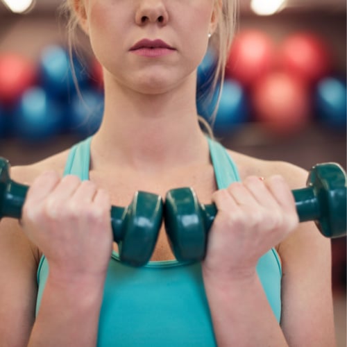 Gros plan sur les mains d'une femme tenant de petits haltères de fitness colorés.