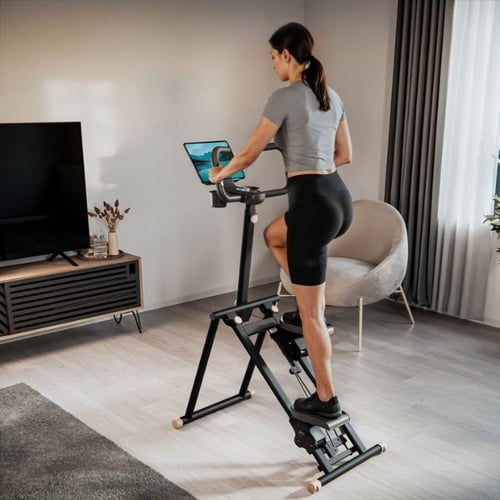 Une femme marche sur un stepper escalier pliable dans le salon en regardant la télévision