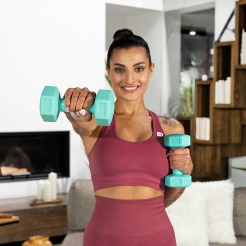 Une femme souriante tient des haltères de fitness bleus dans ses mains