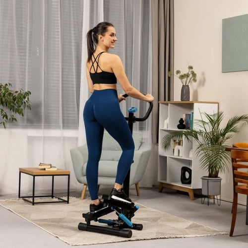 Voici la traduction de la balise alt en français :  Une femme s'entraîne sur un stepper dans le salon, est tournée dos, porte des leggings bleus.