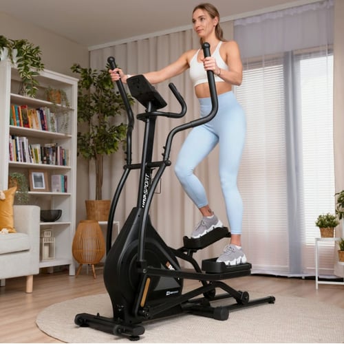 Femme en leggings bleus s'exerçant sur une grande machine elliptique à la maison