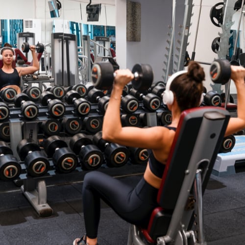 Une femme effectue un Arnold Press avec des haltères à la salle de sport.