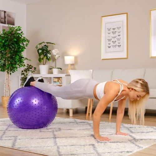 Une femme blonde s'appuie sur le sol avec ses mains, ses jambes sont posées sur une balle de gymnastique et elle effectue l'exercice swiss ball pike