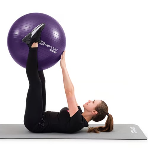Une femme fait l'exercice du dead bug avec un ballon de gym.   
